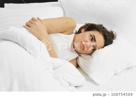Portrait of woman feeling unwell, lying in bed with menstrual pain, stomach ache, frowning and looking sad Portrait of woman feeling unwell, lying in bed with menstrual pain, stomach ache, frowning and looking sad 108754509