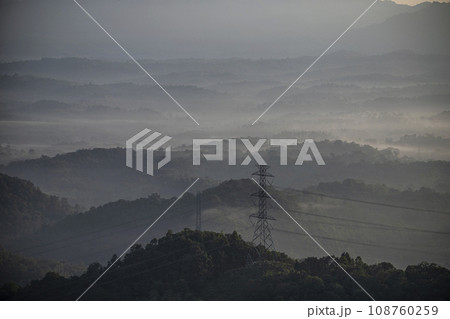 Mist flows through a valley and There are lines of electrical transmission towers high on the mountain. 108760259