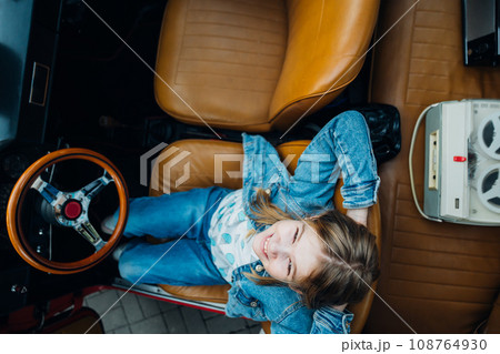 Teen girl in denim clothes driving a red vintage retro car with a folding roof. Teen girl in denim clothes driving a red vintage retro car with a folding roof. 108764930