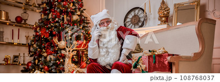 Santa Claus talking on phone sitting neat christmas tree with gifts. New year and Merry Christmas Santa Claus talking on phone sitting neat christmas tree with gifts. New year and Merry Christmas 108768037