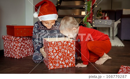 Two smiling boys in pajamas and Santa caps got excited after opening Christmas gifts and presents at morning 108770287