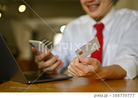 Smiling businessman hand holding credit bank card and using mobile phone for doing online banking transaction Smiling businessman hand holding credit bank card and using mobile phone for doing online banking transaction 108770777