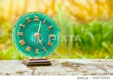 Clock with emerald dial. Gold numbers and arrows. Old stone among greenery Clock with emerald dial. Gold numbers and arrows. Old stone among greenery 108770893