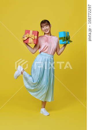Portrait of beautiful, stylish woman emotionally posing with present boxes over yellow background. Portrait of beautiful, stylish woman emotionally posing with present boxes over yellow background. 108772297