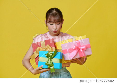 Portrait of beautiful, stylish woman emotionally posing with present boxes over yellow background. Portrait of beautiful, stylish woman emotionally posing with present boxes over yellow background. 108772302