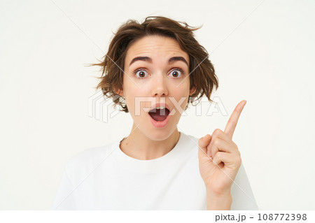 Excited girl has an idea, thinks of solution, pointing one finger and smiling, standing over white background Excited girl has an idea, thinks of solution, pointing one finger and smiling, standing over white background 108772398