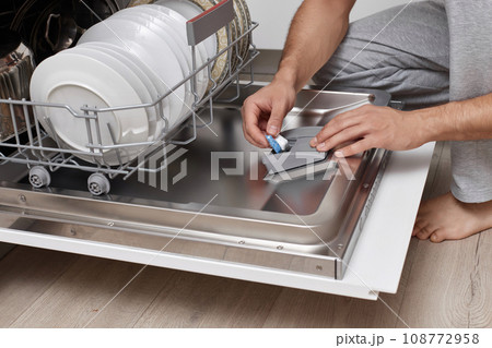handsome man putting detergent tablet into dishwasher in kitchen 108772958