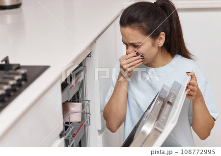 woman smells strange and terrible smell coming from dishwasher machine in kitchen 108772995