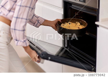 female hands put pan of plum dough into the modern kitchen oven. 108773042