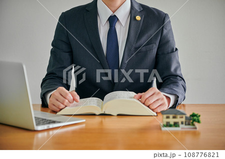 実家の空き家問題について六法全書を見て調査する男性弁護士 108776821