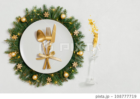 Festive table setting with Christmas wreath and golden decorations on white background with copy space. Happy new year. Space for text. Top view, flat lay. Festive table setting with Christmas wreath and golden decorations on white background with copy space. Happy new year. Space for text. Top view, flat lay. 108777719
