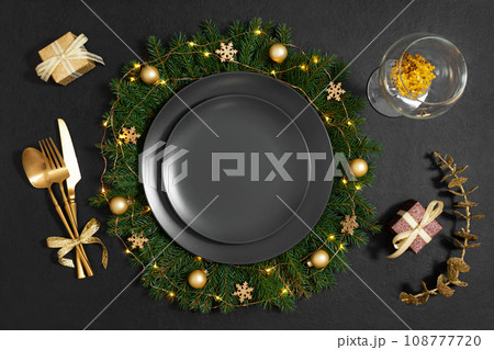 Empty black plate in Christmas wreath with gold decor on black background. Beautiful New Year serving. Space for text. Winter concept. Top view, flat lay. Empty black plate in Christmas wreath with gold decor on black background. Beautiful New Year serving. Space for text. Winter concept. Top view, flat lay. 108777720