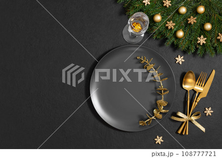 Christmas table setting with fir branches, golden decorations on black background. Empty black plate for design. Happy new year. Space for text. Top view, flat lay. 108777721