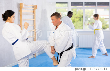 Woman and man in kimono and belts sparring during karate training Woman and man in kimono and belts sparring during karate training 108778014