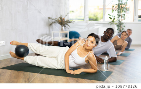 Young woman practicing pilates with soft ball in group Young woman practicing pilates with soft ball in group 108778126