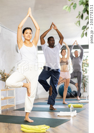 Happy woman in sportswear exercising with group active multinational people during yoga class in fitness center, standing in 108778151