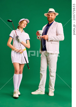 Gorgeous father and daughter. Dad in white smart casual outfit with cup of coffee ands dressed like golf player girl teenager on green background. 108778633