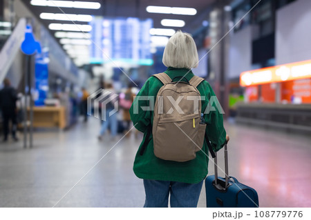 Senior Caucasian woman in international airport, using mobile smartphone and checking flight at the flight information board 108779776