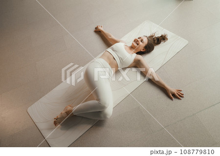 A girl in white clothes does yoga lying on a rug indoors 108779810
