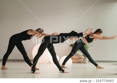 A group of girls in black doing yoga poses indoors. Women are engaged in fitness A group of girls in black doing yoga poses indoors. Women are engaged in fitness 108779865