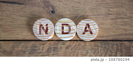 Wooden small circles with letters NDA on wood background. Concept image. 108780294