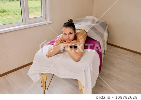 Massage table with European woman in her 20s who is lying on her stomach. Massage table with European woman in her 20s who is lying on her stomach. 108782628