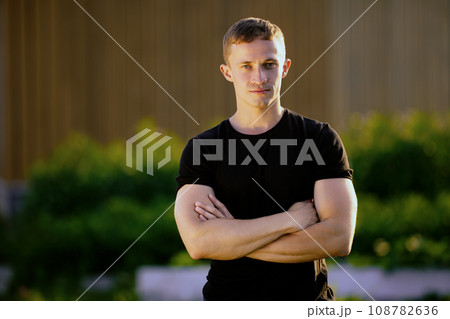 Medium shot portrait photo of man with his arms crossed, warm lighting on summer evening at sunset. 108782636