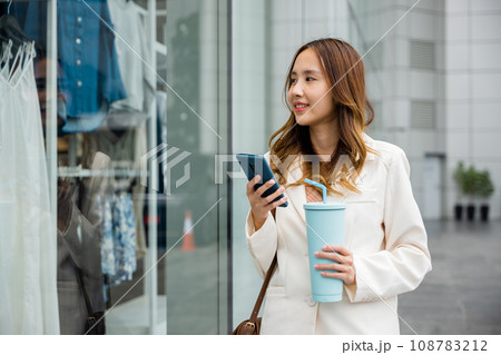 Busy lifestyle in the city ,young woman holding a tumbler mug and smartphone while multitasking. Hot beverage and smart technology in one. Busy lifestyle in the city ,young woman holding a tumbler mug and smartphone while multitasking. Hot beverage and smart technology in one. 108783212
