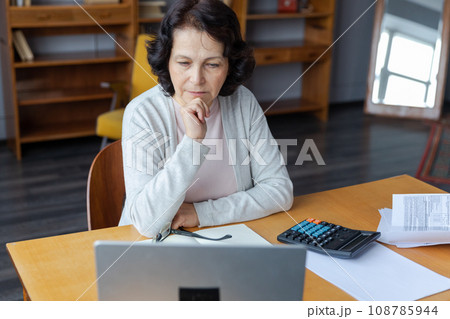 Confident stylish european middle aged senior woman using laptop at home. Stylish older mature 60s lady sitting at table looking at computer screen typing chatting reading writing email 108785944