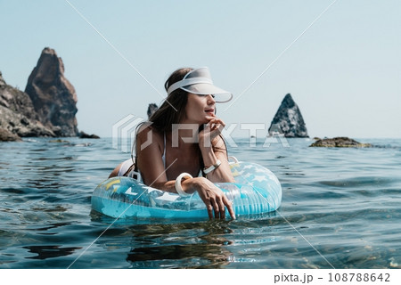 Woman summer sea. Happy woman swimming with inflatable donut on the beach in summer sunny day, surrounded by volcanic mountains. Summer vacation concept. Woman summer sea. Happy woman swimming with inflatable donut on the beach in summer sunny day, surrounded by volcanic mountains. Summer vacation concept. 108788642