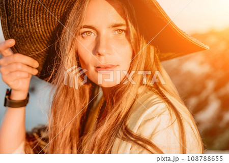 Portrait of happy young woman wearing summer black hat with large brim at beach on sunset. Closeup face of attractive girl with black straw hat. Happy young woman smiling and looking at camera at sea. Portrait of happy young woman wearing summer black hat with large brim at beach on sunset. Closeup face of attractive girl with black straw hat. Happy young woman smiling and looking at camera at sea. 108788655