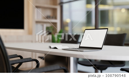 A white-screen laptop mockup on a white meeting table in a modern, minimalist meeting room. A white-screen laptop mockup on a white meeting table in a modern, minimalist meeting room. 108790548