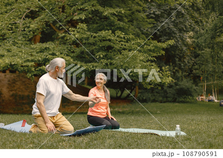Senior man and woman with yoga mats standing at park. Positive mature man and his elderly wife have a fitness or yoga class in nature. Wellness and healthy lifestyle on retirement. 108790591