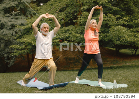 Senior man and woman with yoga mats standing at park. Positive mature man and his elderly wife have a fitness or yoga class in nature. Wellness and healthy lifestyle on retirement. 108790594
