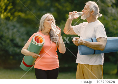 Senior man and woman with yoga mats standing at park. Positive mature man and his elderly wife after fitness or yoga class in nature. Wellness and healthy lifestyle on retirement. 108790620