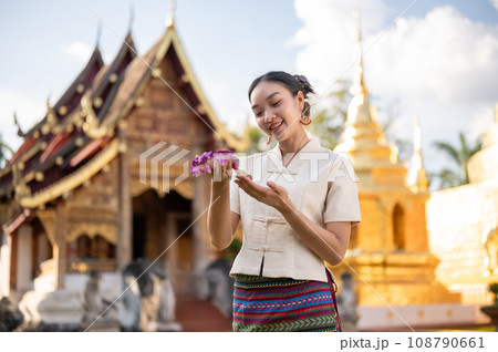 A charming Thai woman in a traditional Thai-Lanna dress is admiring a beautiful garland in her hand. A charming Thai woman in a traditional Thai-Lanna dress is admiring a beautiful garland in her hand. 108790661