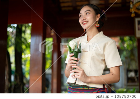 A beautiful Thai-Asian woman with a flower for pay respect to the image of the Buddha in a temple. 108790700