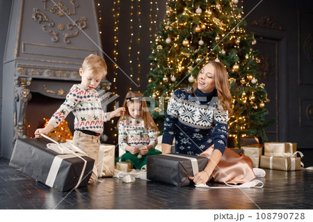 Young mother, little daughter and son in studio posing for a photo. Woman and kids wearing knitted sweaters with Christmas prints. Family celebrating Christmas together. 108790728