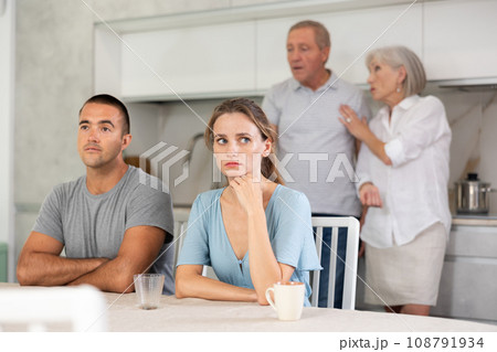 Portrait of an offended married couple in home kitchen, which mature family members reprimand. Family conflict 108791934