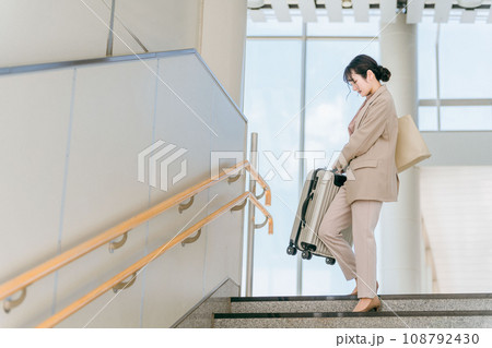階段で重い荷物を持つ女性(駅・空港) 階段で重い荷物を持つ女性(駅・空港) 108792430