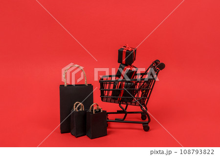 Black shopping cart with paper bags and gift boxes on red background, copy space. black friday concept Black shopping cart with paper bags and gift boxes on red background, copy space. black friday concept 108793822