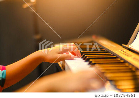 Close-up of a little student's hand playing the piano. Happy young Asian girl learning and practicing the piano. Selective focus. Close-up of a little student's hand playing the piano. Happy young Asian girl learning and practicing the piano. Selective focus. 108794861