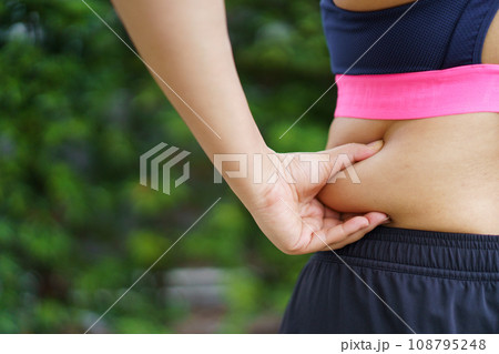 Unhealthy overweight Asian fat woman catching on her big belly and arm close up, woman concerned about her fat and body shape problem. Unhealthy overweight Asian fat woman catching on her big belly and arm close up, woman concerned about her fat and body shape problem. 108795248