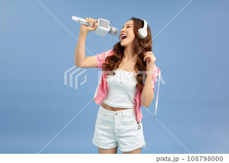 Portrait of a beautiful mature woman singing into microphone with headphones on blue background Portrait of a beautiful mature woman singing into microphone with headphones on blue background 108798000