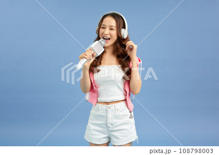 Carefree happy asian woman singing in microphone, listen music in headphones, blue background 108798003