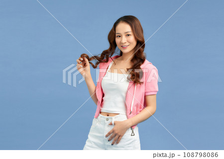 Portrait of a cute positive Asian woman in pink hoodie standing over blue background 108798086