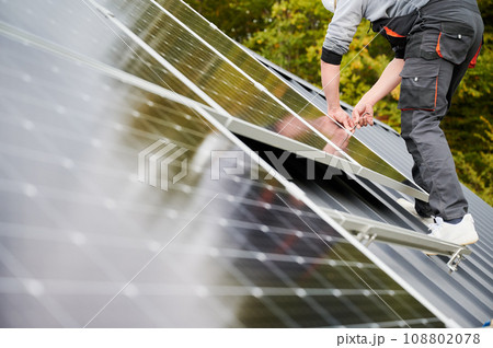 Man technician mounting photovoltaic solar panels on roof of house. Close up view of engineer installing solar module system with help of hex key. Concept of alternative, renewable energy. 108802078