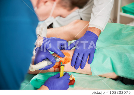 Close up of doctors making injection in knee and ultrasound diagnostics in hospital. Men wearing robe and latex gloves, holding boy knee. Concept of medicine and taking care of health. 108802079