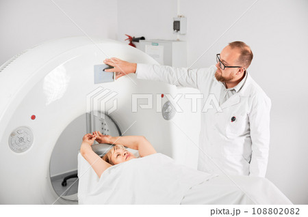Medical computed tomography or MRI scanner. Male radiologist presses MRI button to examine female patient. Concept of healthcare and modern diagnostics. 108802082