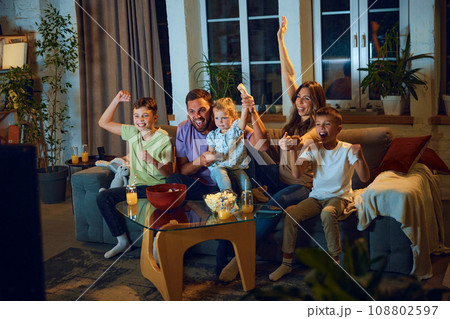 Family watching football match at home. Mother, father and children sitting on ouch at home and cheering up sport team 108802597